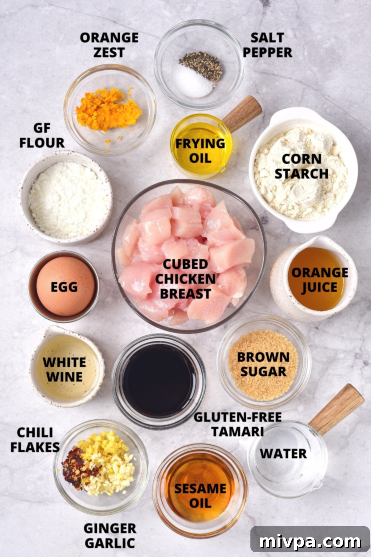Easy Gluten-Free Orange Chicken Recipe (Dairy-Free) All the fresh ingredients for a homemade gluten-free orange chicken recipe neatly arranged on a marble cutting board.