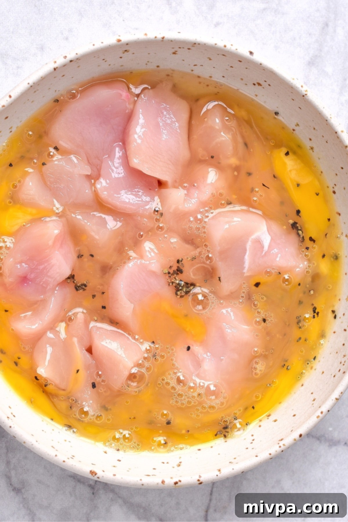 Orange chicken gluten-free recipe Diced chicken pieces thoroughly coated in a whisked egg mixture, resting in a pristine white bowl.