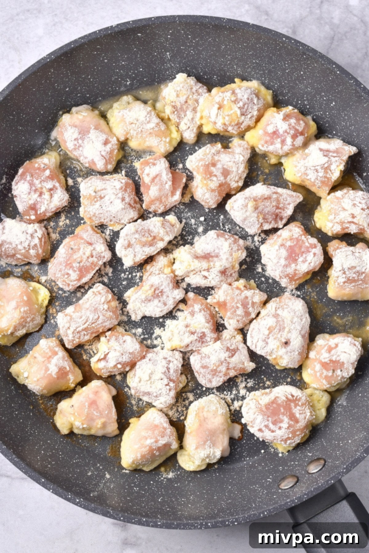 Gluten-Free Dairy-Free Orange Chicken Flour-coated chicken pieces carefully placed in a hot skillet, ready for frying.
