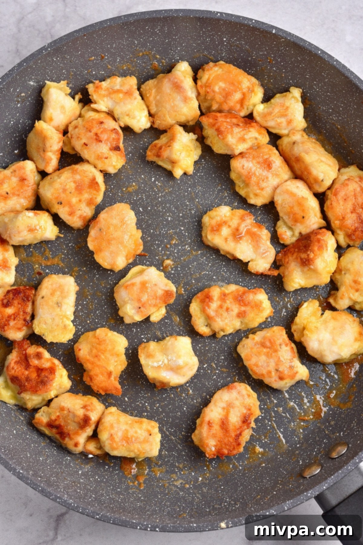 Easy Gluten-Free Orange Chicken Recipe (Dairy-Free) Golden brown and crispy fried chicken pieces in a large skillet, looking perfectly cooked.