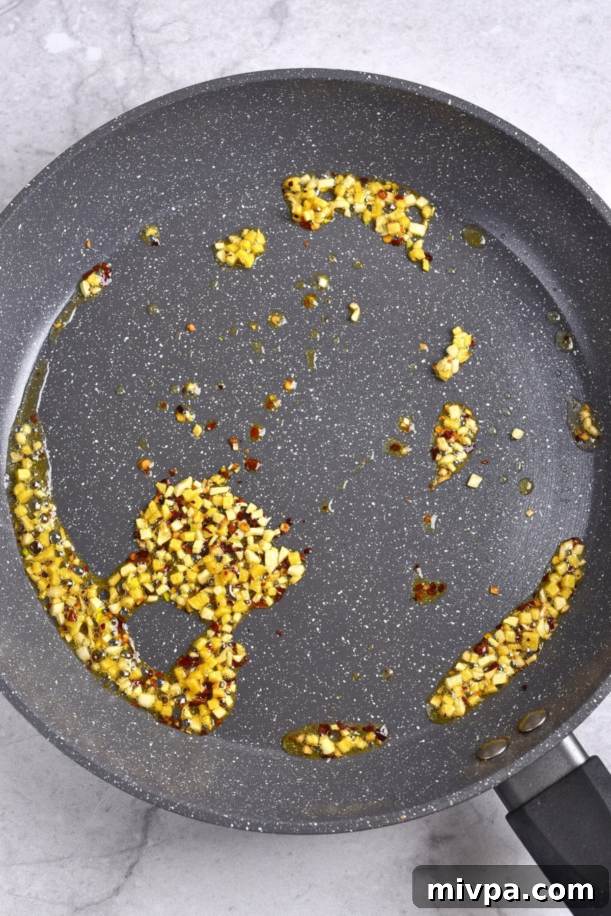 Copycat Panda Express Orange Chicken Gluten-Free Minced garlic and ginger, along with chili flakes, sizzling in a skillet, creating a fragrant base for the sauce.