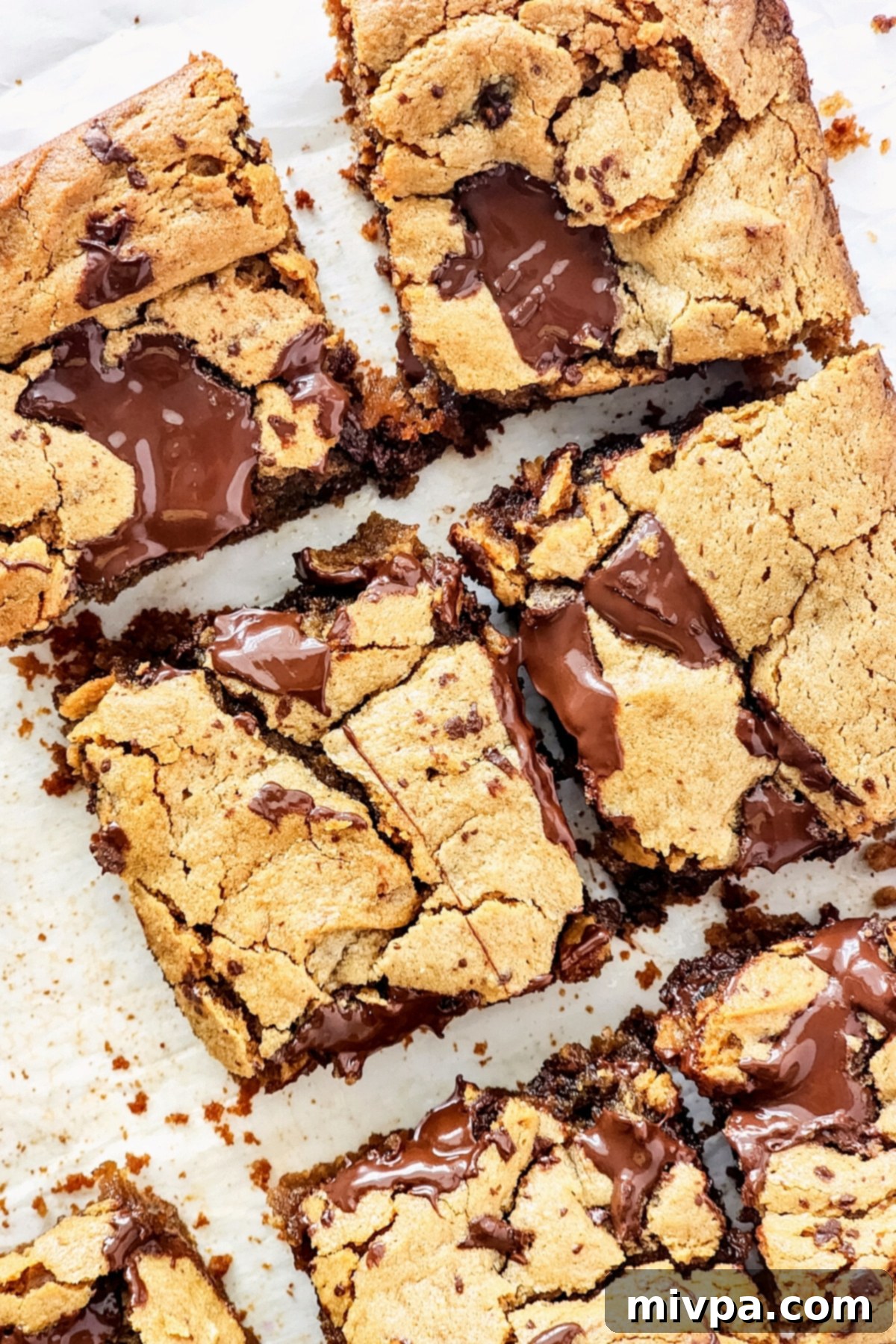 Up close shot of golden brown gluten-free peanut butter blondies on parchment paper, revealing their chewy texture and chocolate chunks.