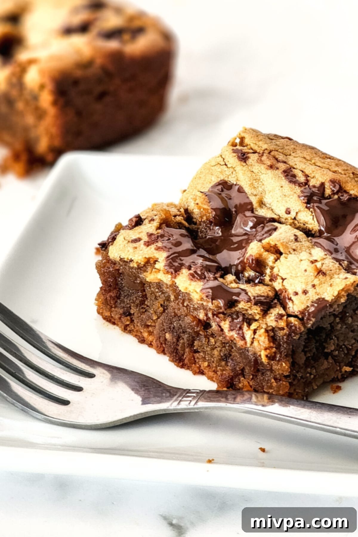 Up close shot of a healthy peanut butter blondie on a white plate, showcasing its soft, moist interior and melted chocolate.