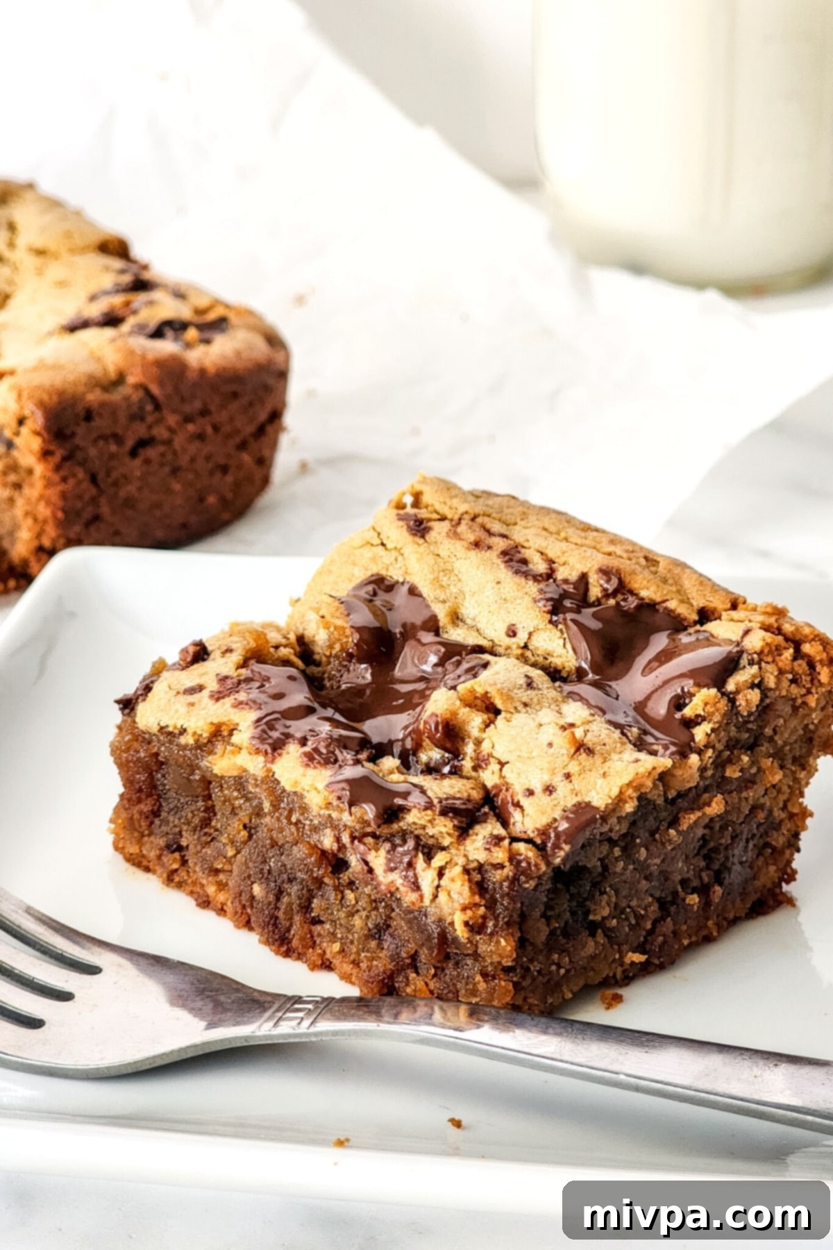 A perfectly sliced, moist peanut butter blondie on a white plate, showcasing its golden hue and visible chocolate pieces.
