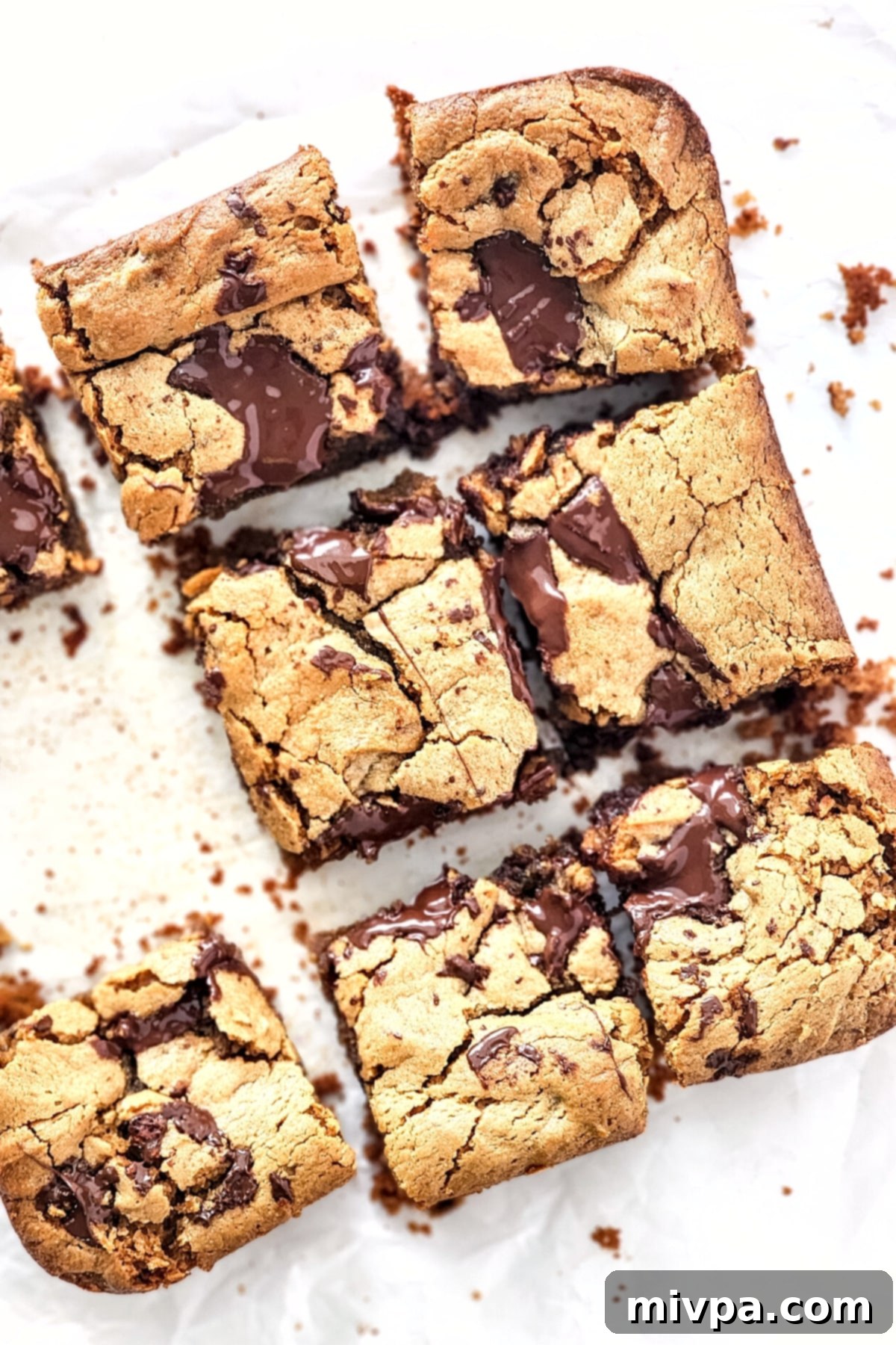 Close-up of golden gluten-free peanut butter cookie bars cooling on parchment paper, showing their soft interiors.