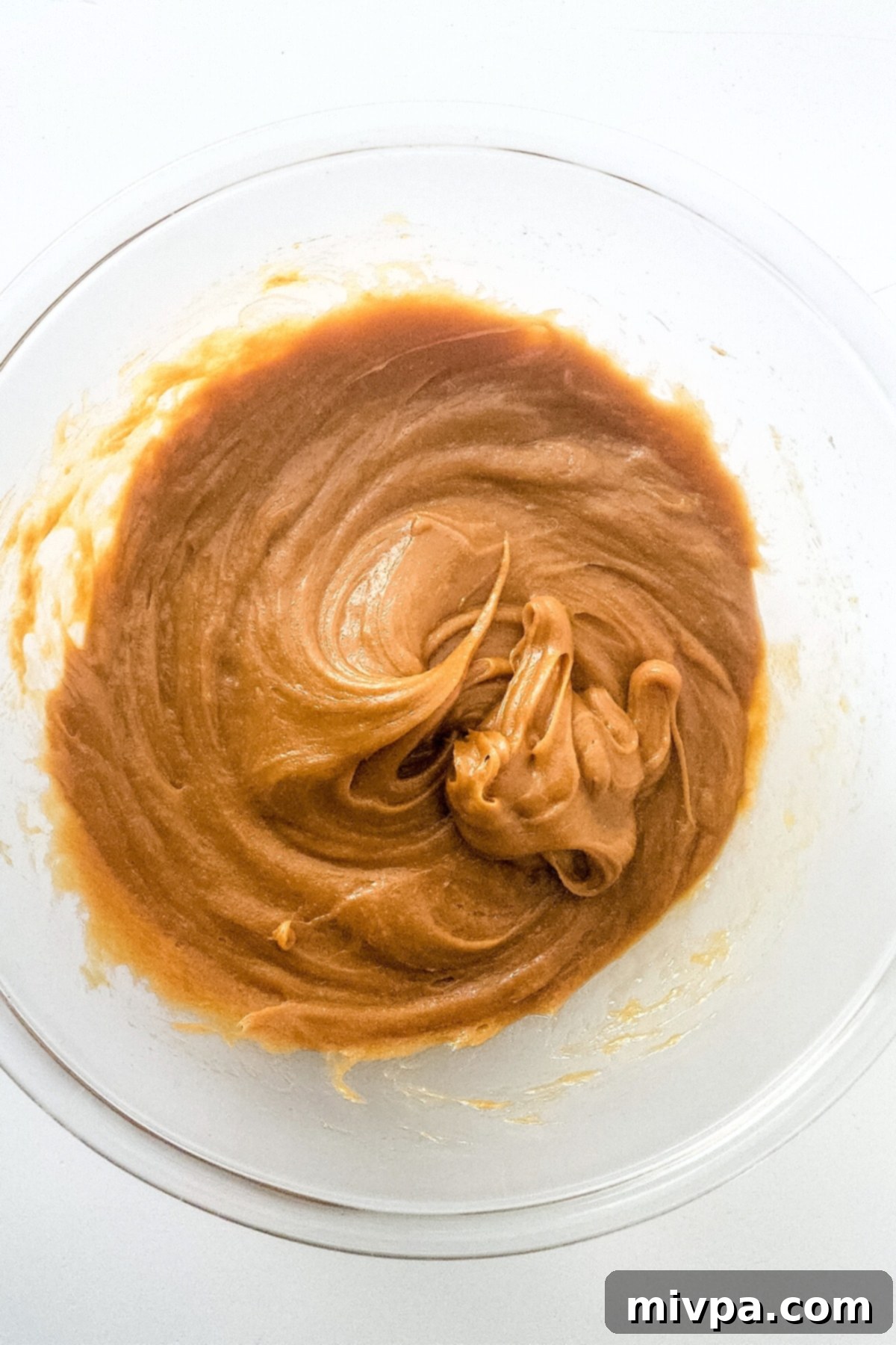 Creamy peanut butter, maple syrup, and eggs whisked together in a clear glass mixing bowl.