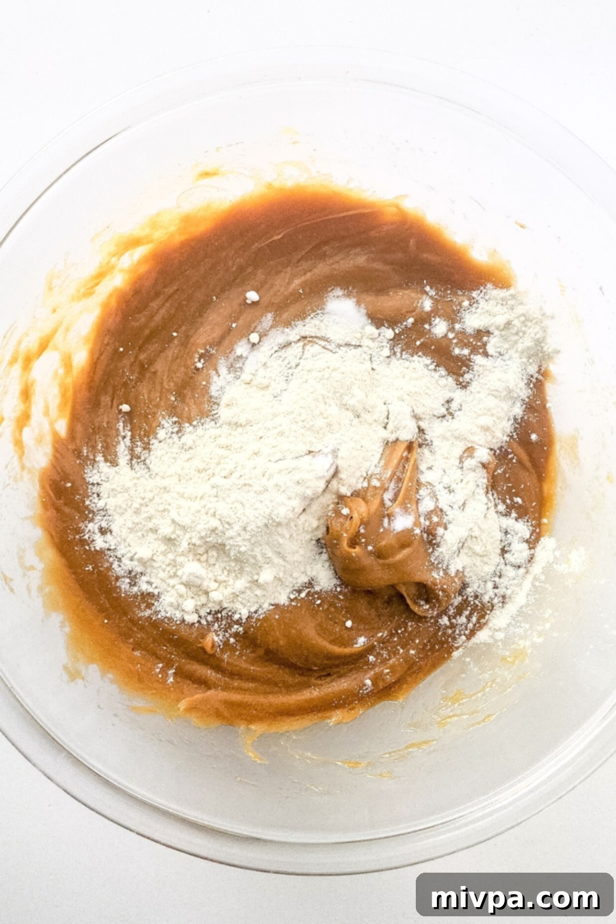 The peanut butter mixture now topped with a mound of gluten-free flour, ready to be mixed.