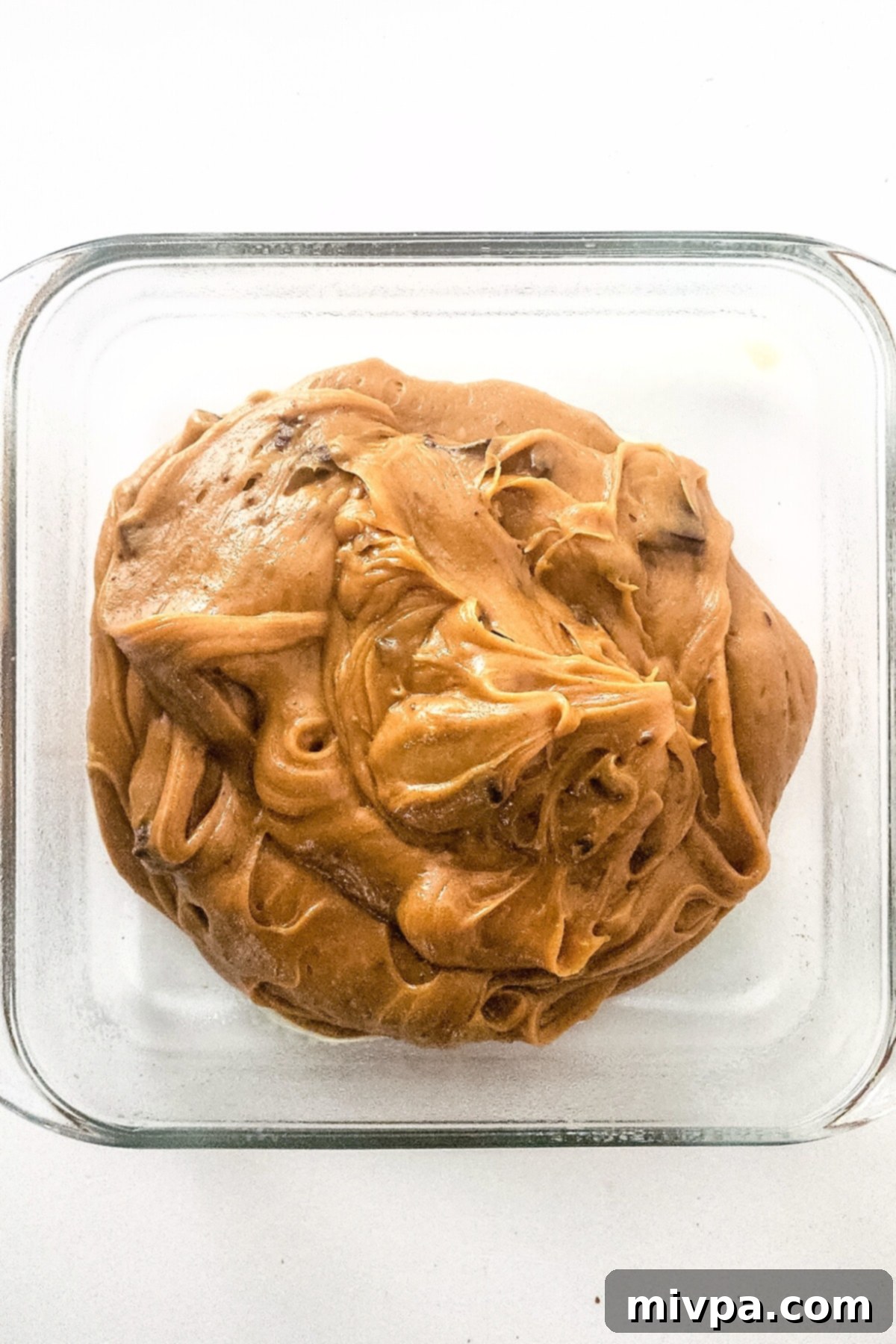 Smooth peanut butter blondie batter evenly spread in a glass baking pan.