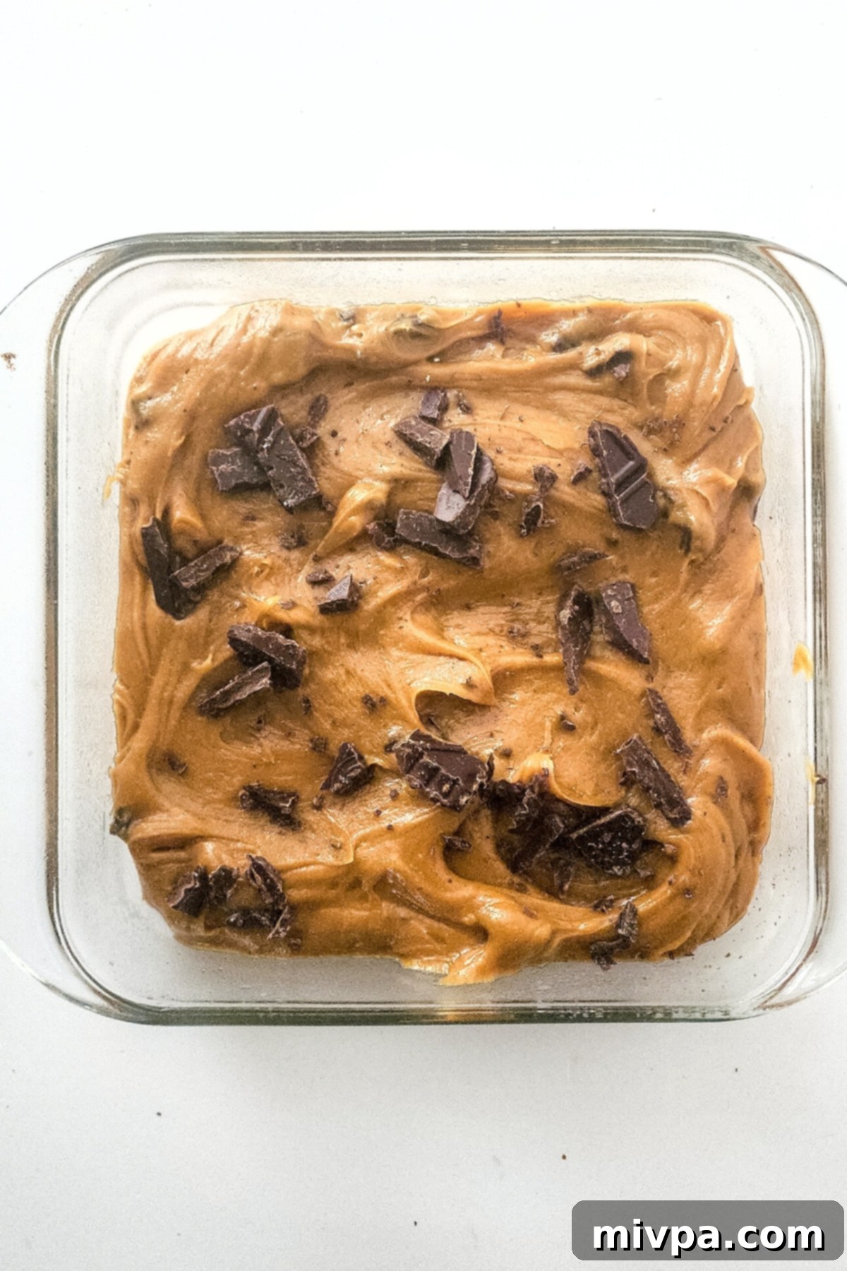 Blondie batter in a glass baking pan, generously topped with extra chocolate chips for a beautiful finish.