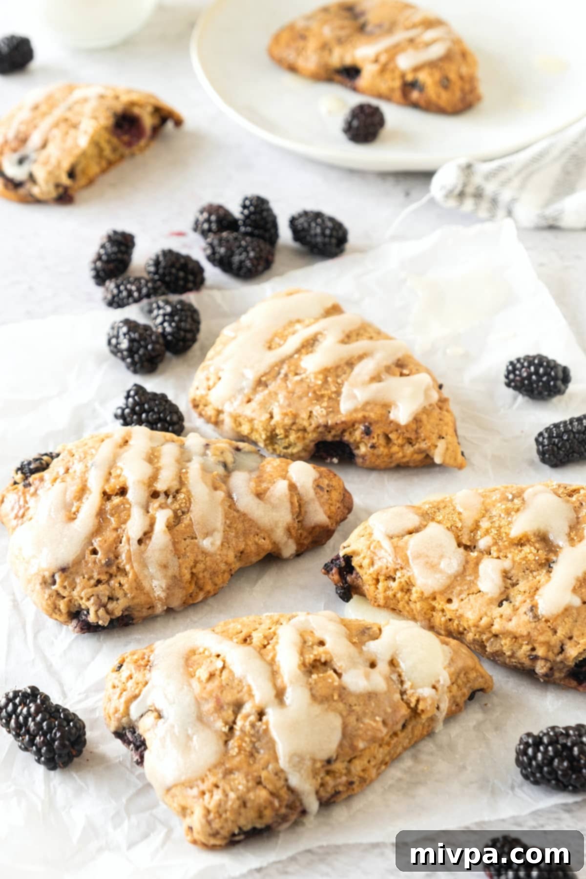 Gluten-Free Blackberry Scones Recipe (Dairy-Free) Glaze drizzled over gluten-free blackberry lemon scones on parchment paper.