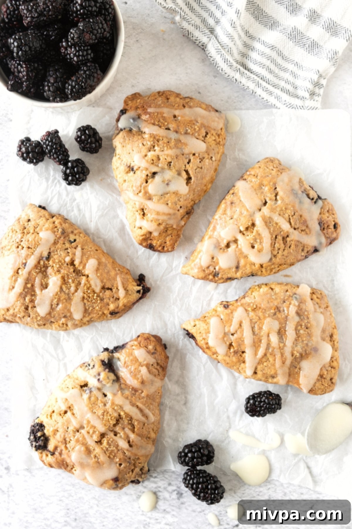 Gluten-Free Blackberry Lemon Scones (Dairy-Free) Top down view of several gluten-free blackberry lemon scones on parchment, with a light dusting of icing.