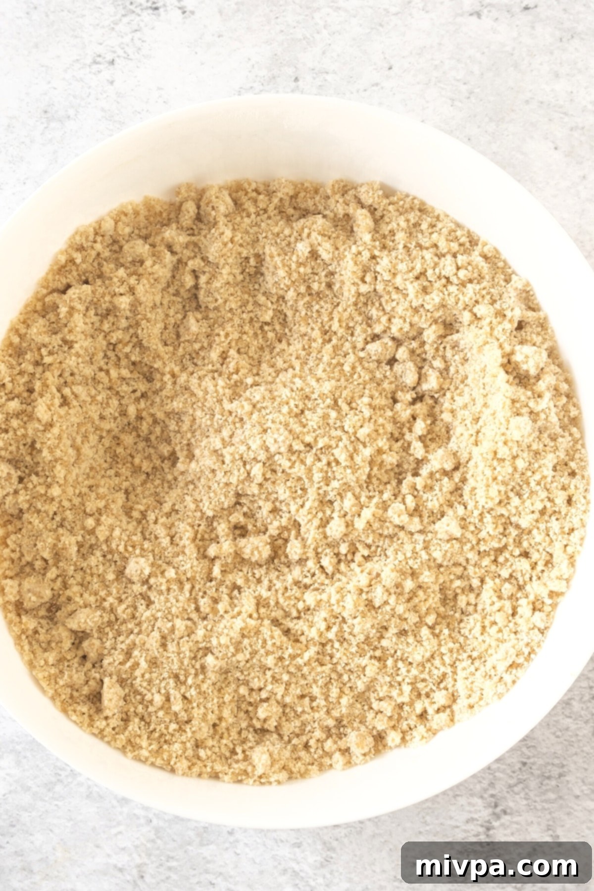 Gluten-Free Lemon Blackberry Scones (Dairy-Free) Butter Cut In Light brown flour mixture with small butter pieces in a white bowl, showing the wet sand texture.