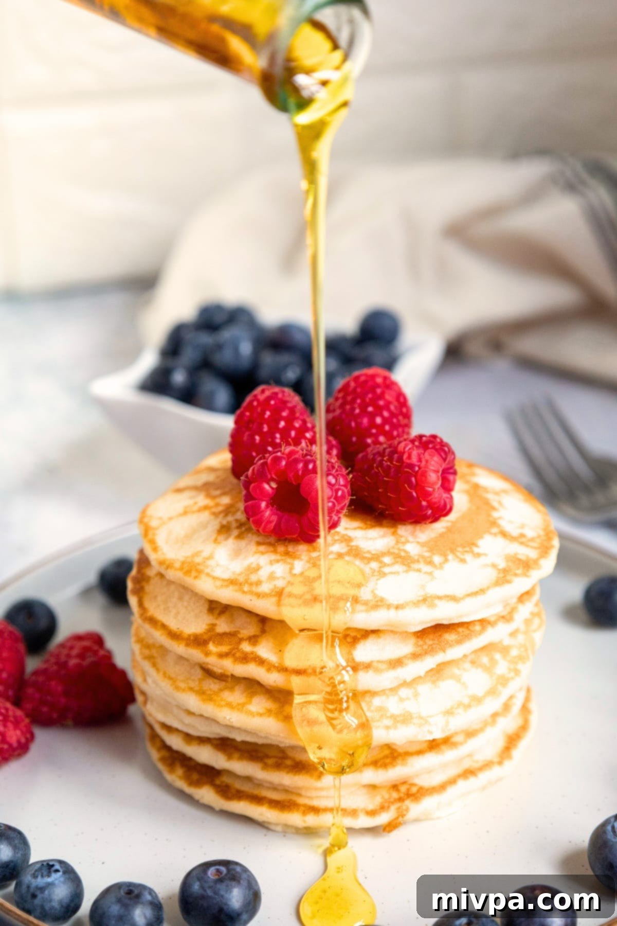 Pouring maple syrup over berry-toped buttermilk pancakes.