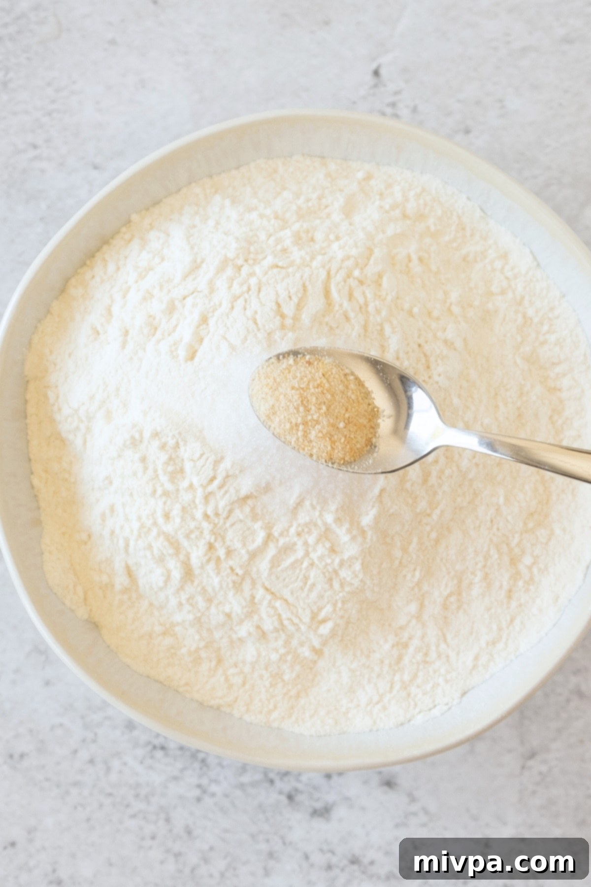 Holding up a spoon of xanthan gum over bowl of dry ingredients.