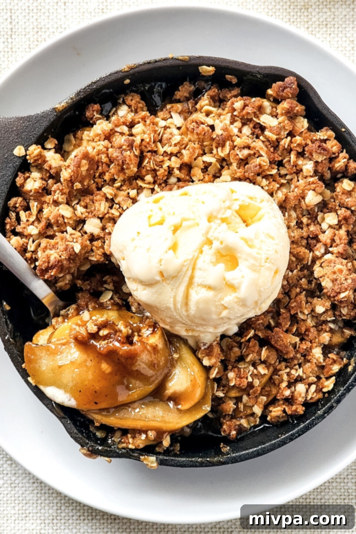Top down view of gluten-free apple crisp in cast iron pan, showing the golden-brown topping and bubbling apple filling.