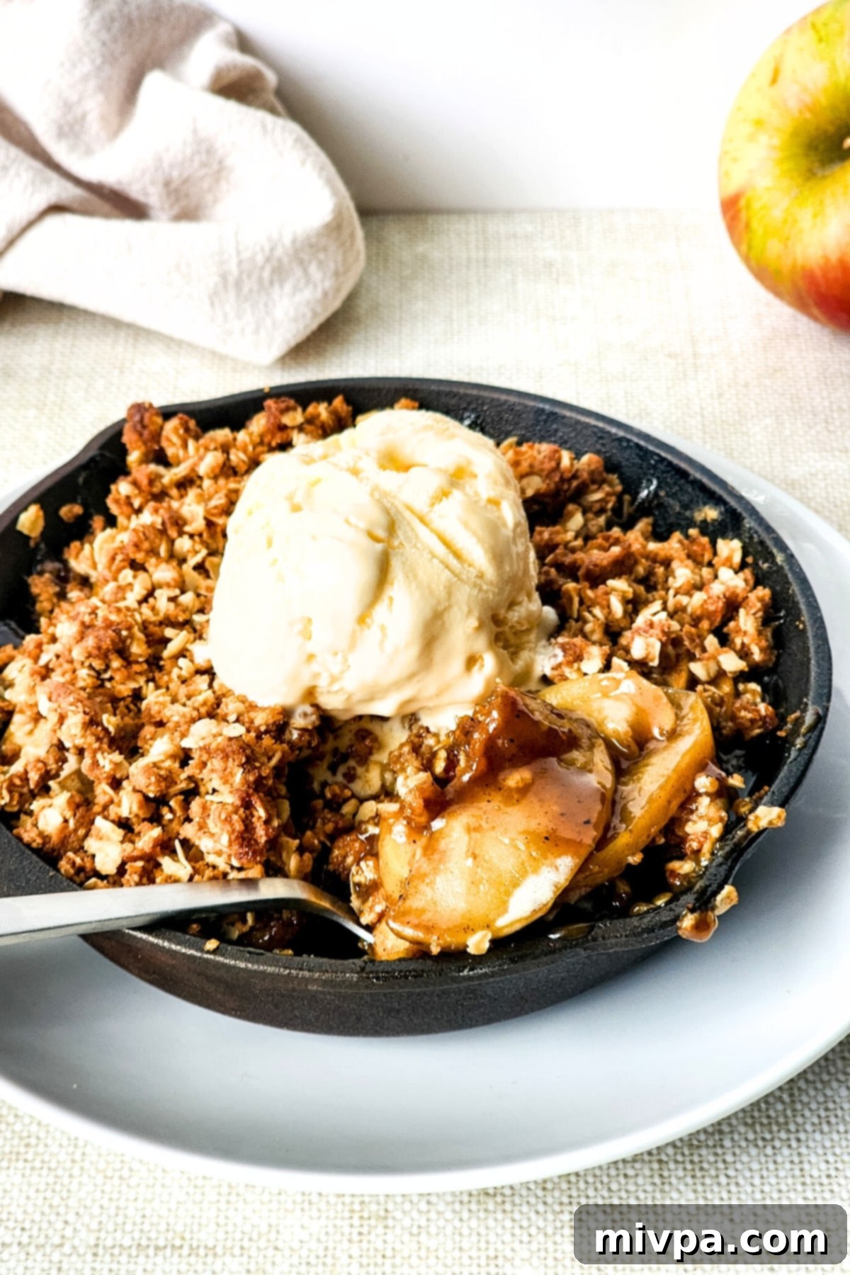 A small skillet with golden-brown apple crisp placed on a white plate, ready to be served.