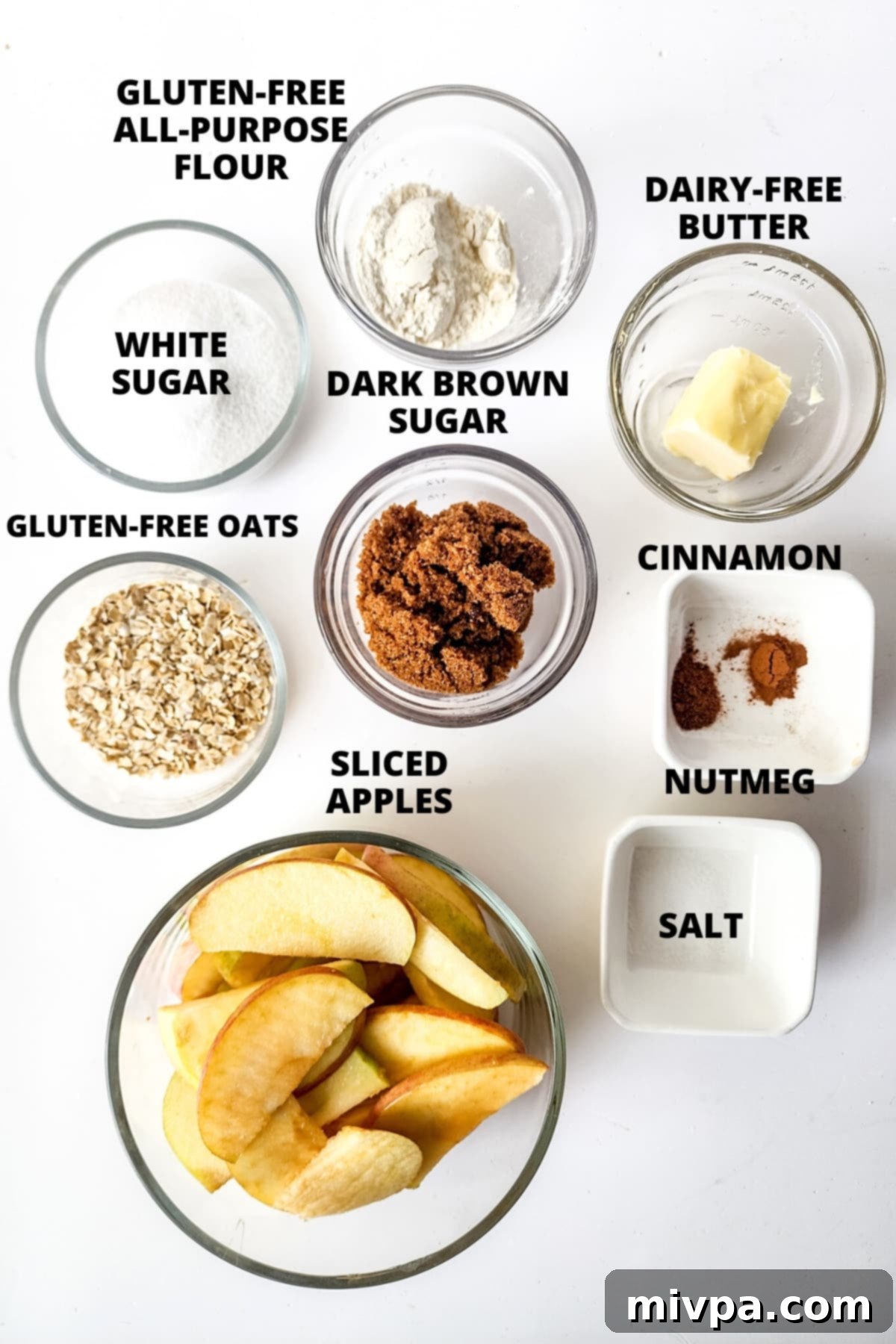 Ingredients for gluten-free apple crisp recipe laid out on a clean white board, showcasing fresh apples, oats, flours, sugars, and spices.