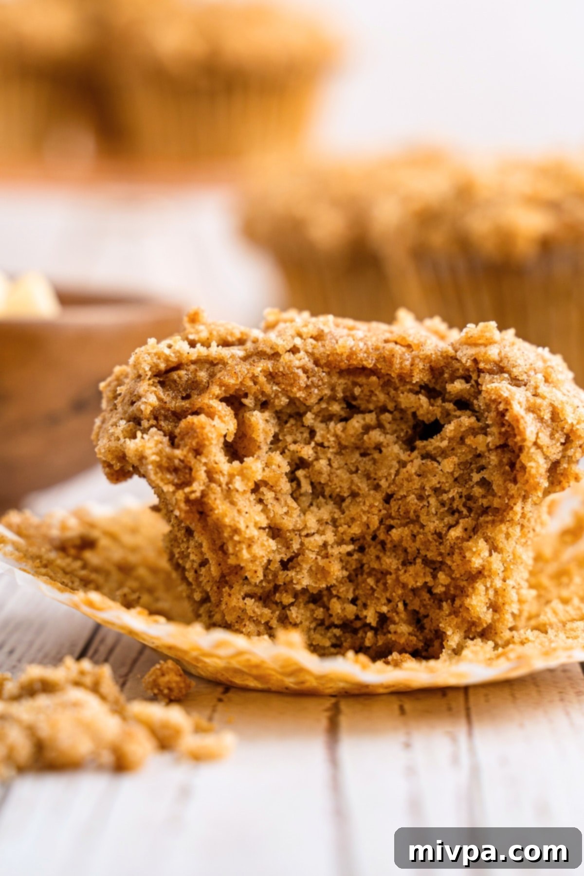 Half-eaten gluten-free applesauce muffin on paper liner.