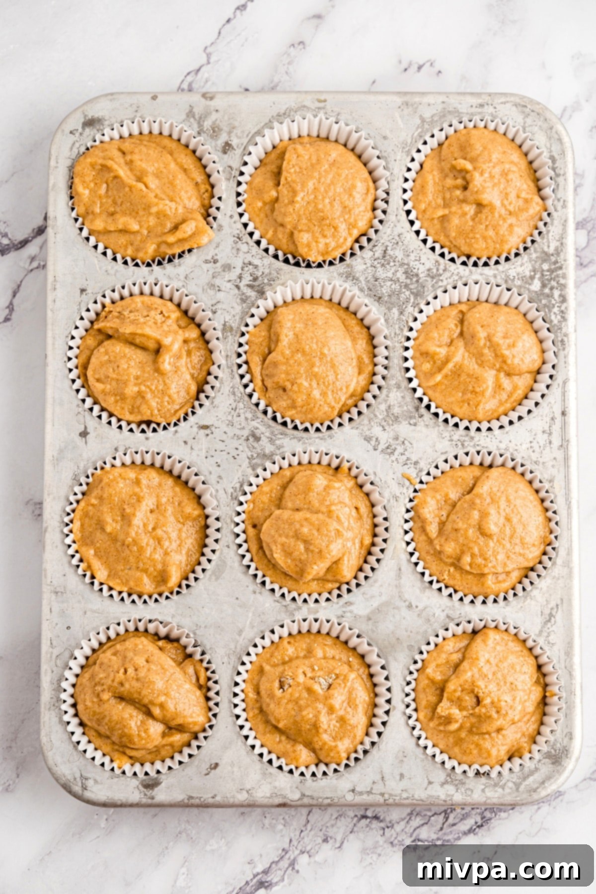 Uncooked muffin batter in muffin liners in muffin pan.