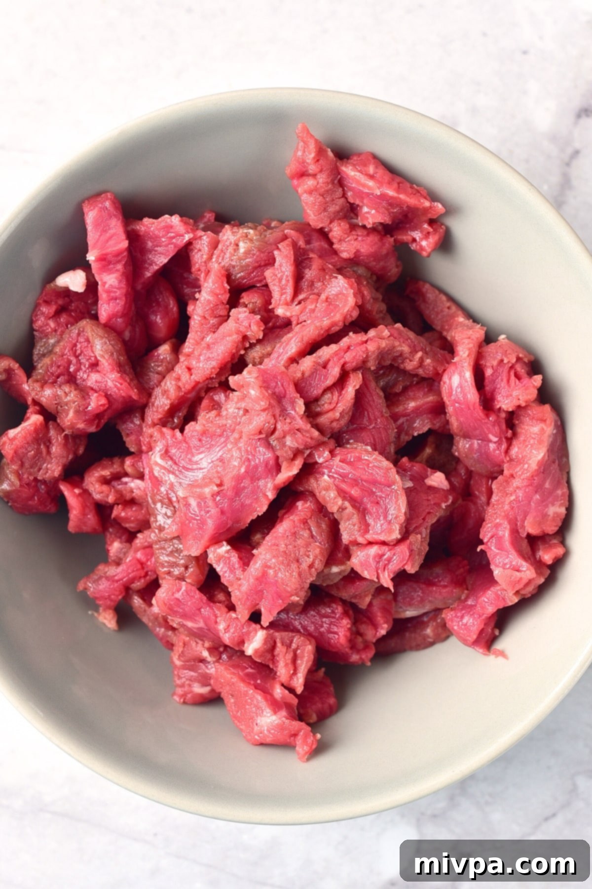 GF Beef Stroganoff (Dairy-Free) Raw beef slices in grey bowl.