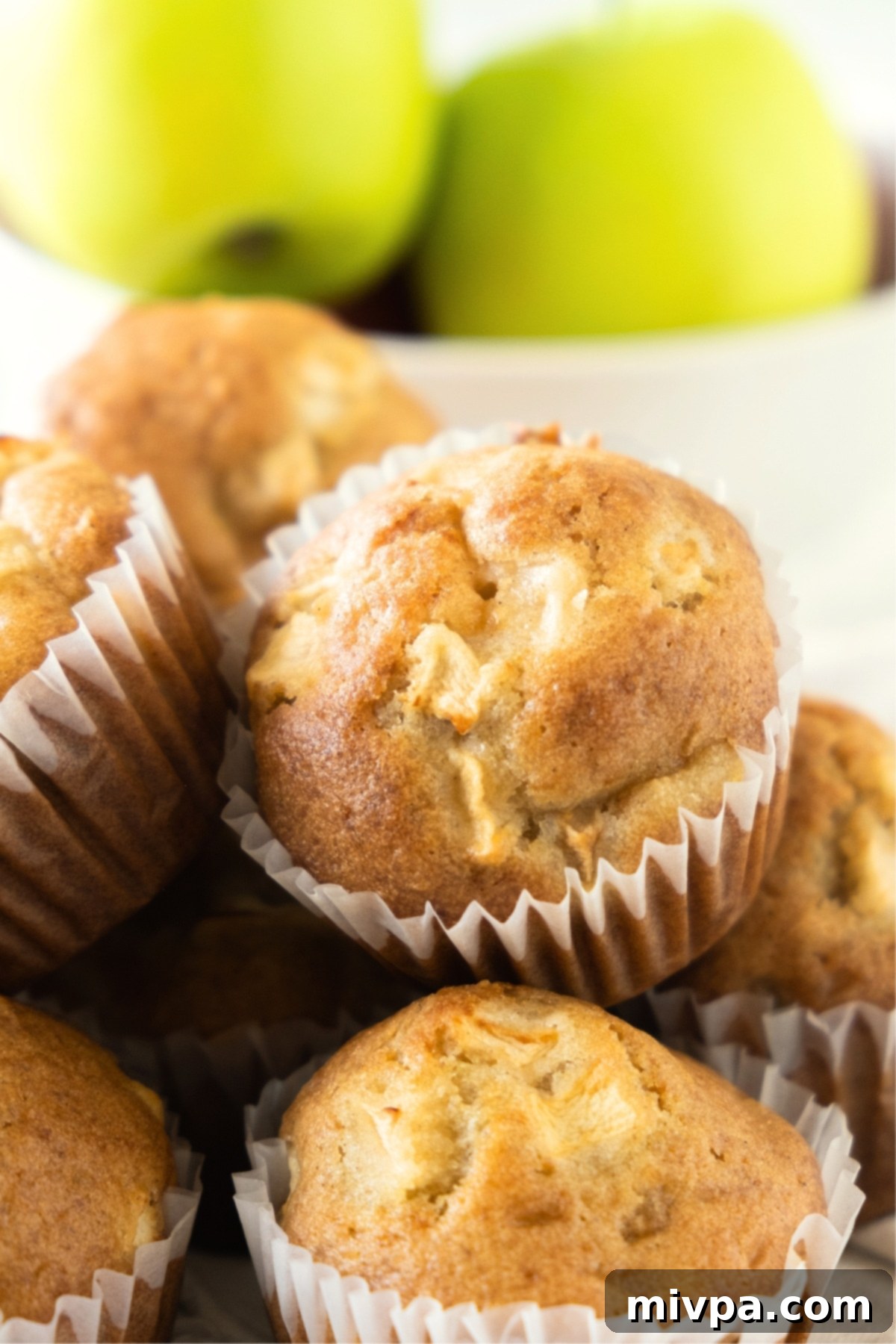A stack of golden brown gluten-free apple muffins in front of vibrant green apples.