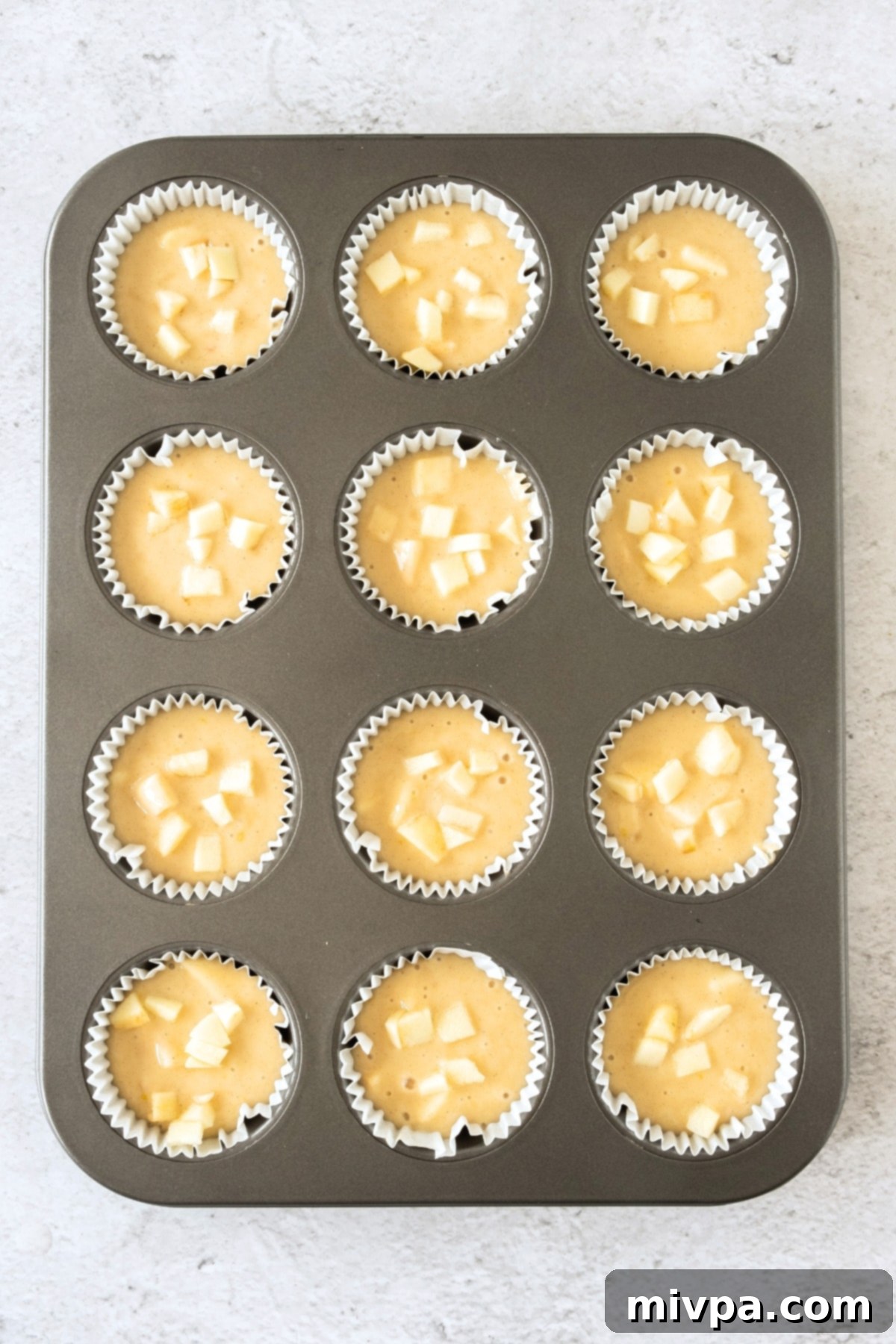 Uncooked muffin batter, topped with extra apple pieces, nestled perfectly in the muffin pan, ready for baking.