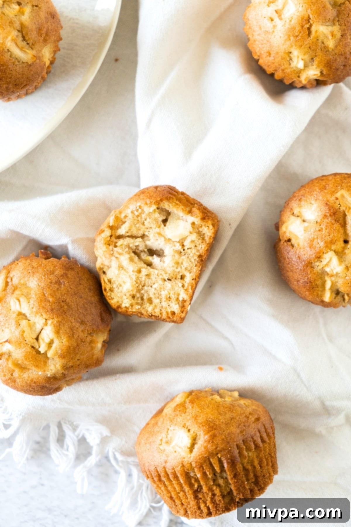 Freshly baked apple muffins artfully arranged on a patterned kitchen towel, exuding warmth and homemade charm.