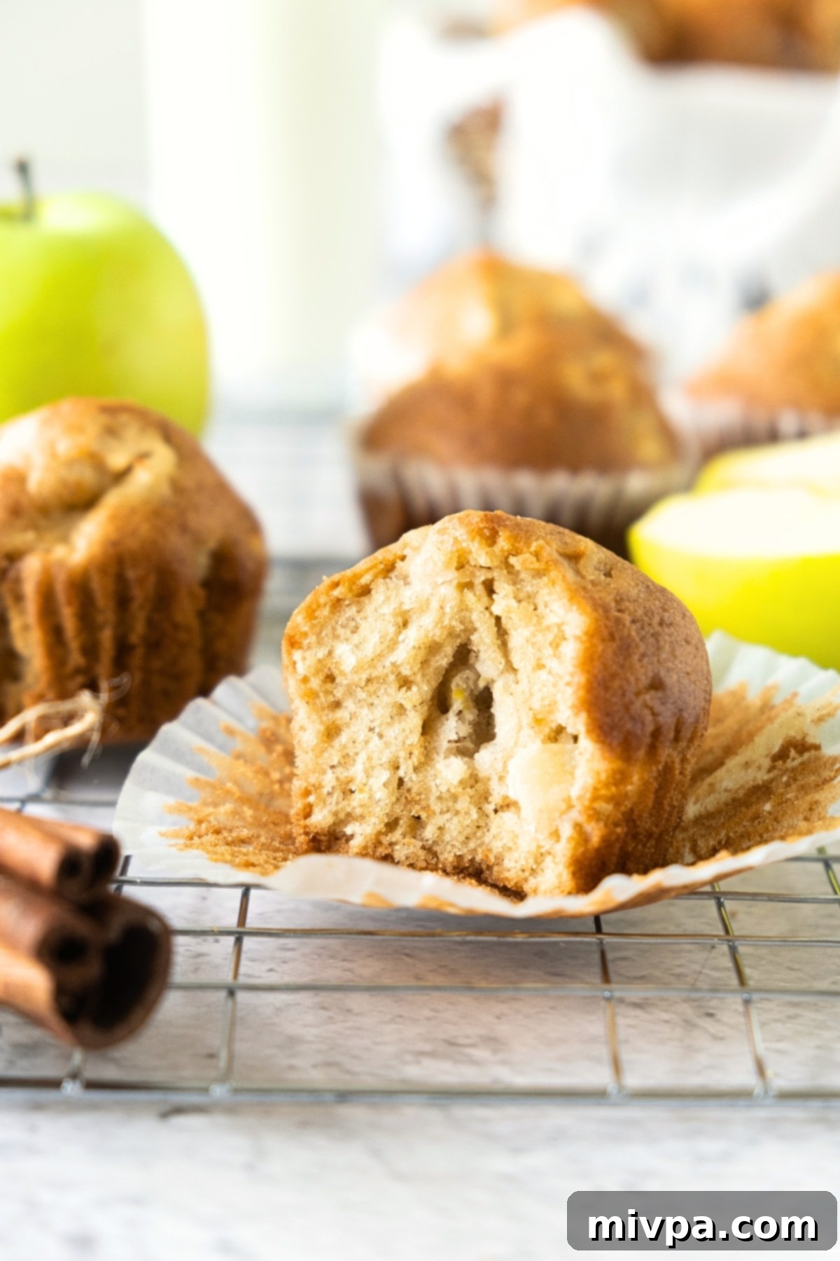 A close-up of a half-eaten gluten-free apple muffin on a wire rack, revealing its soft interior.