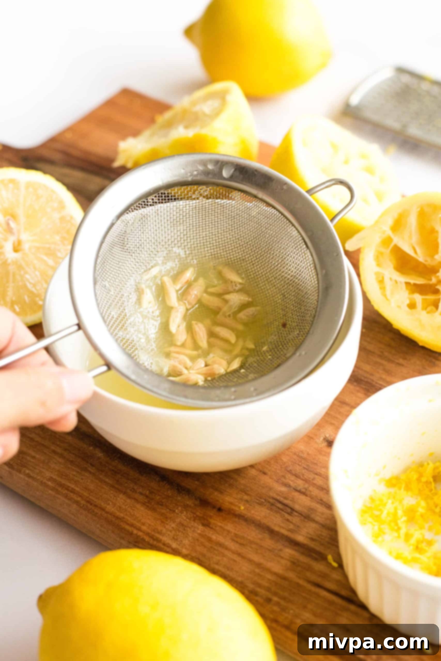 Separating lemon seeds from freshly squeezed lemon juice using a small strainer, ensuring no bitterness.
