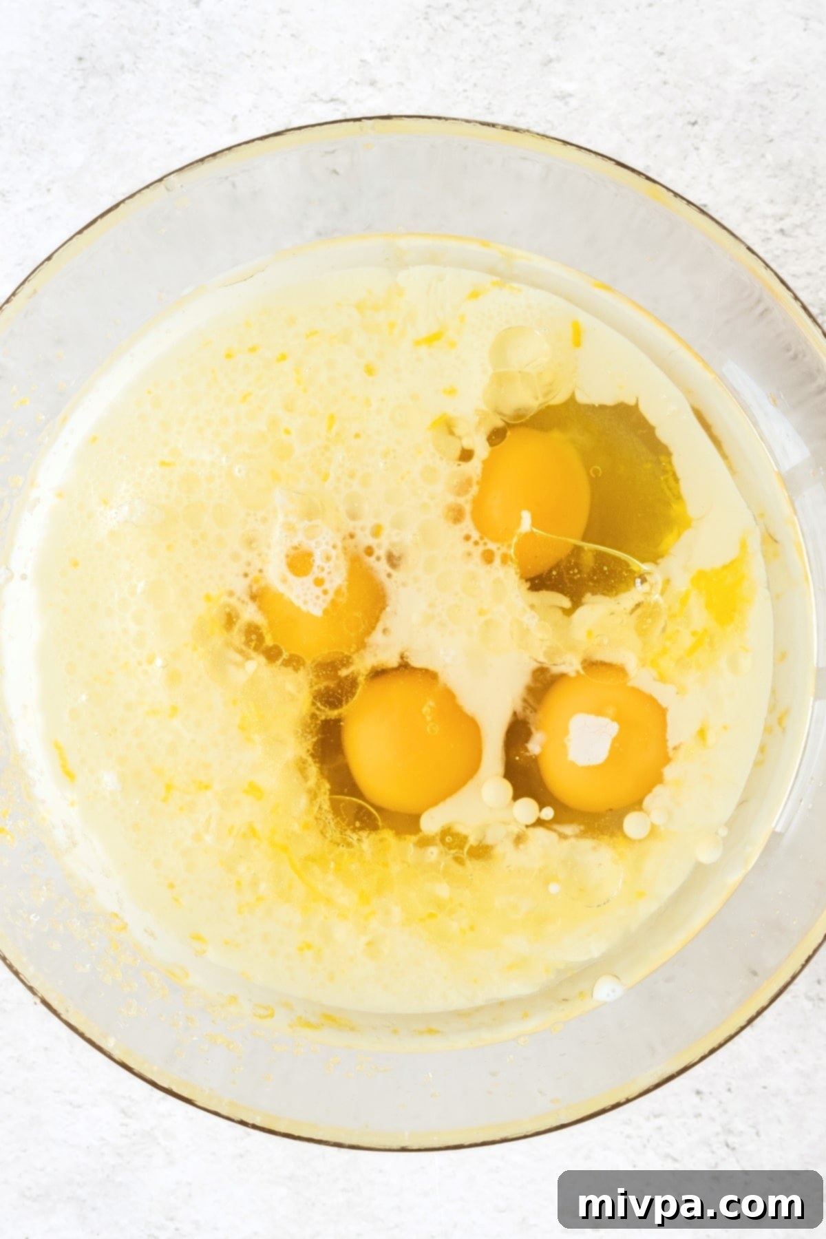 A bowl of muffin batter with eggs, lemon juice, and almond milk added, ready for whisking.