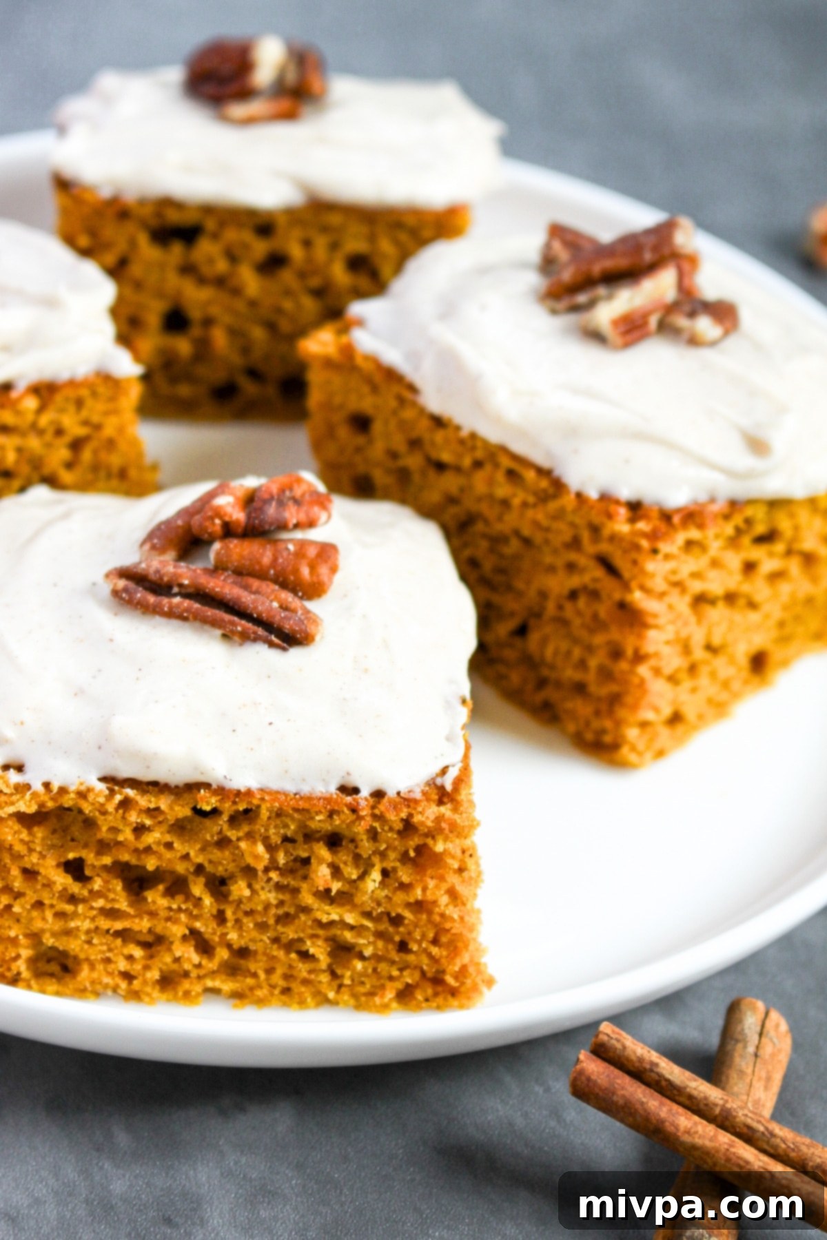 Pieces of gluten-free pumpkin cake squares on white plate, topped with cinnamon cream cheese frosting and pecans.