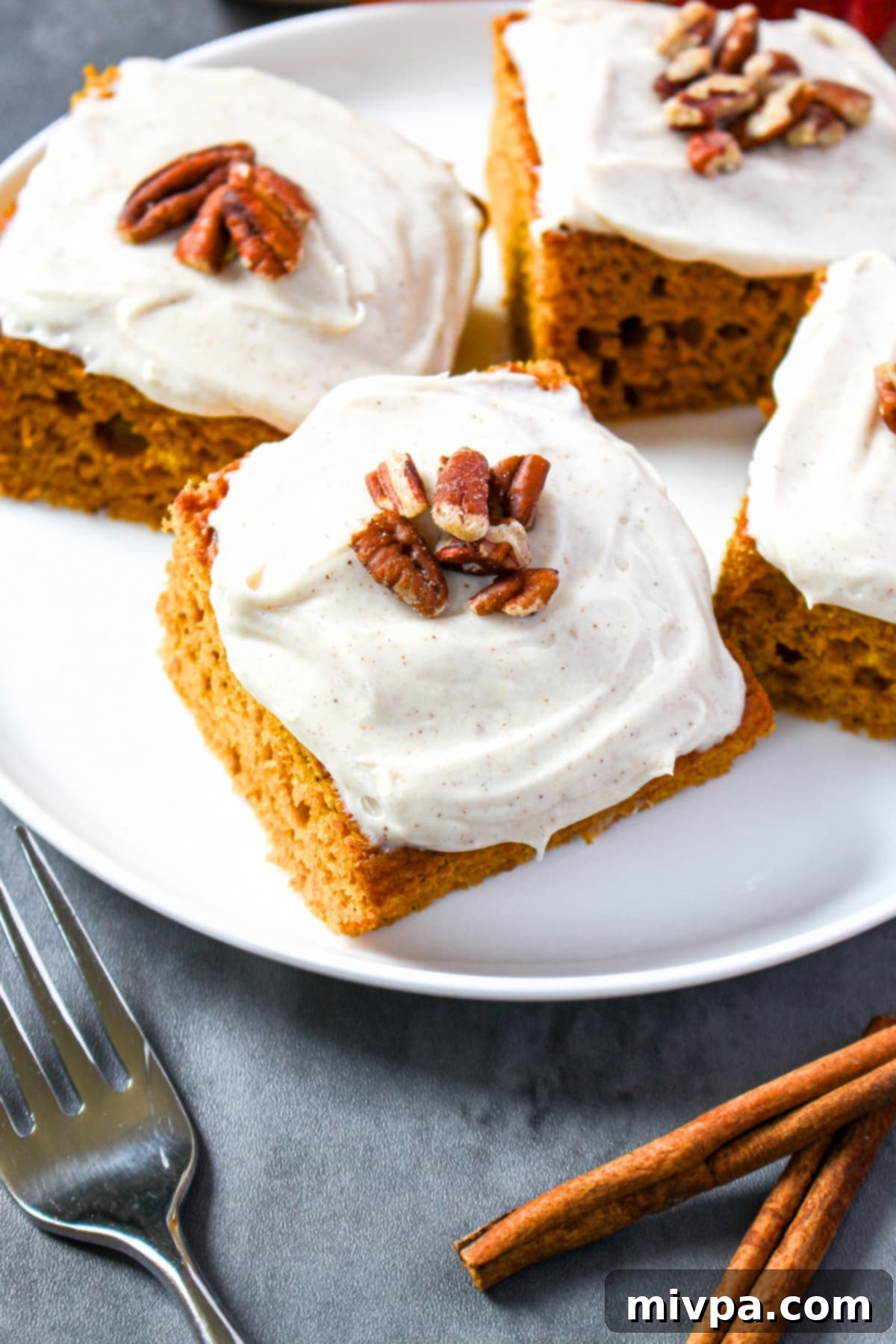Gluten-free pumpkin cake squares topped with frosting and pecans on a serving plate.