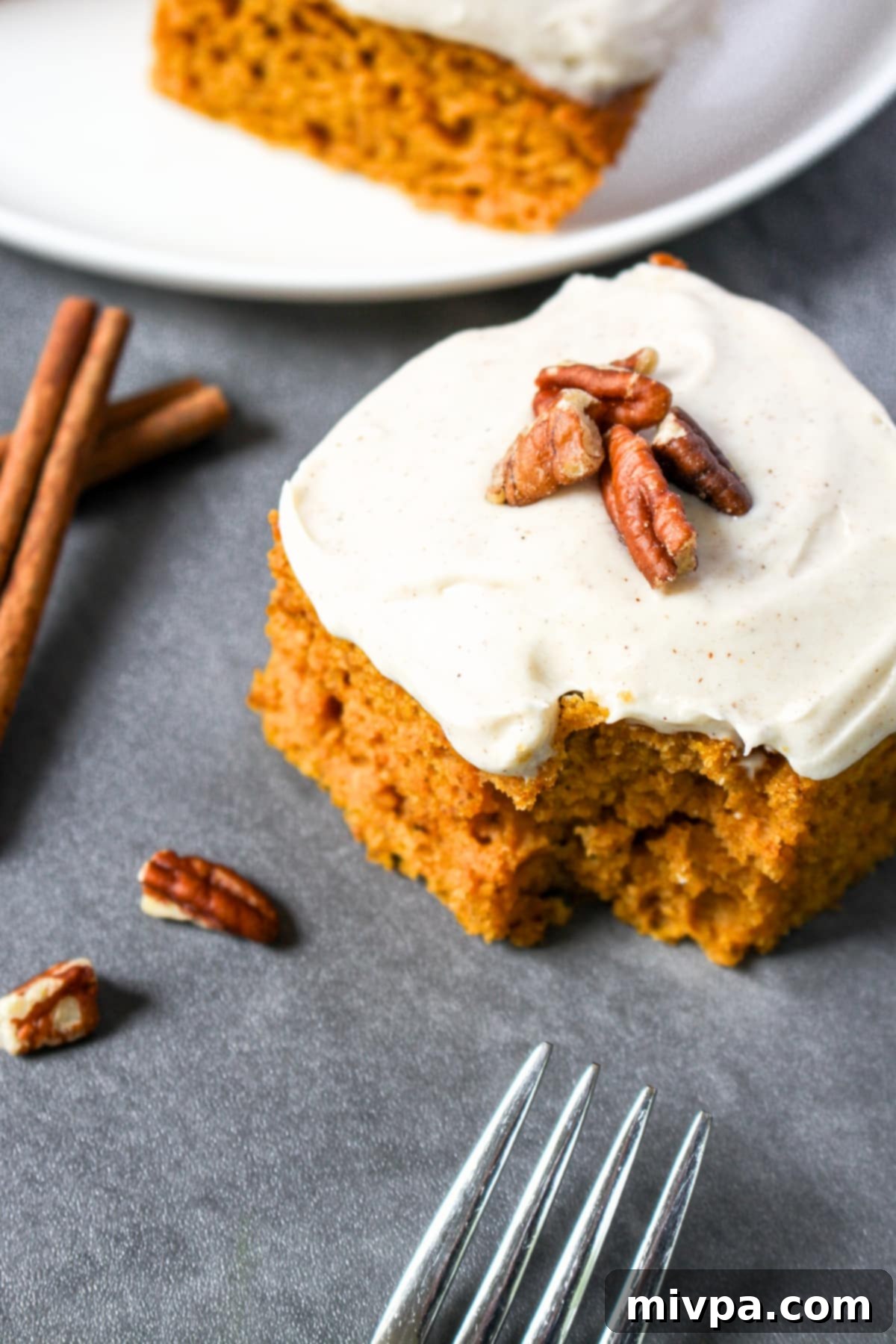 Half-eaten square of gluten-free pumpkin cake with creamy cinnamon cream cheese frosting, showing the texture.