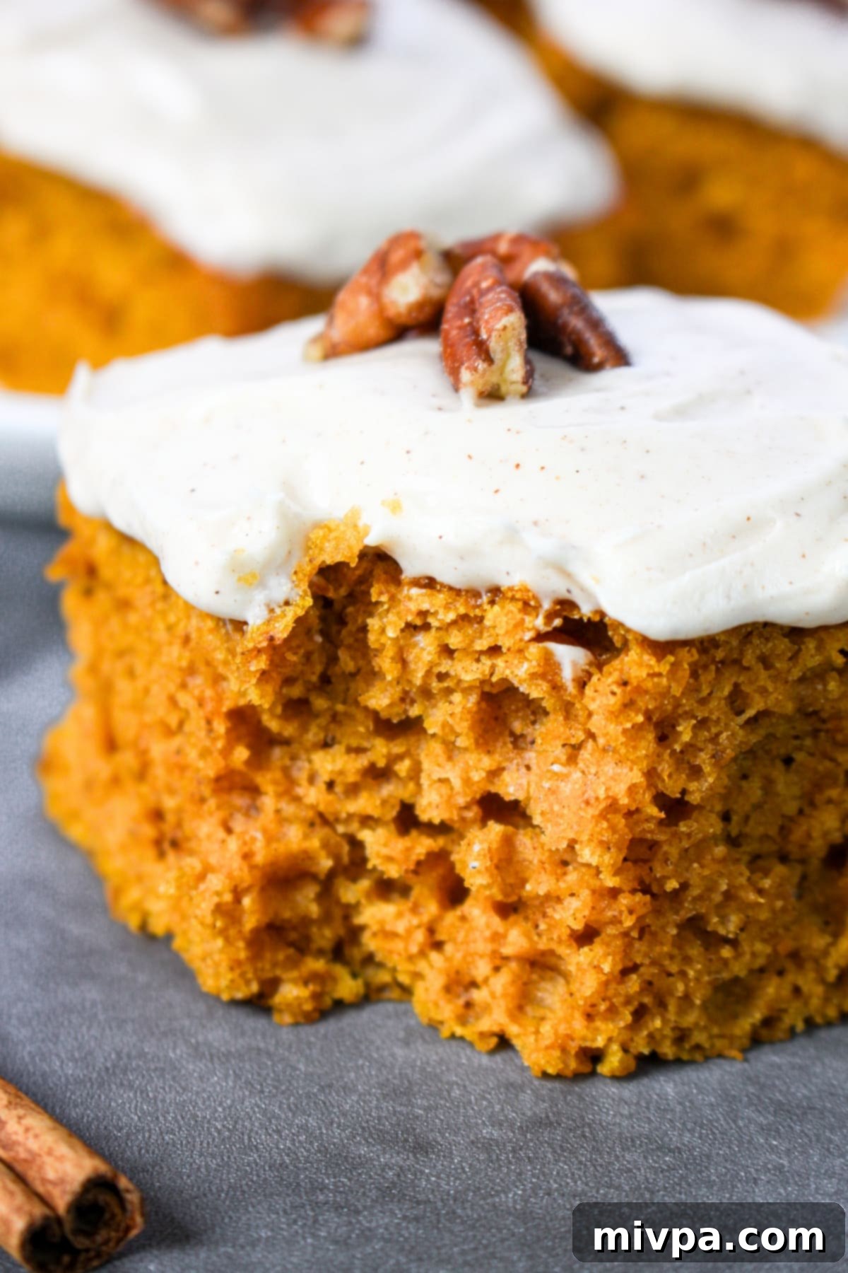 Up close shot of a slice of moist pumpkin cake with a bite taken out, showing the tender crumb and thick frosting.