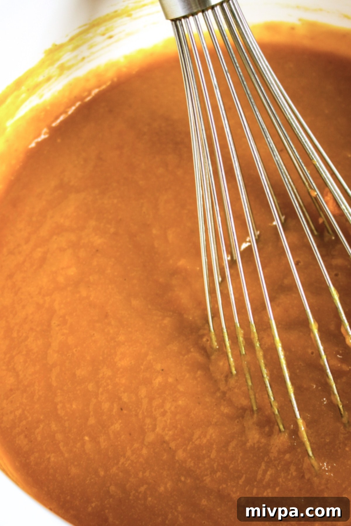 A bowl of wet pumpkin cake mixture being whisked smooth.