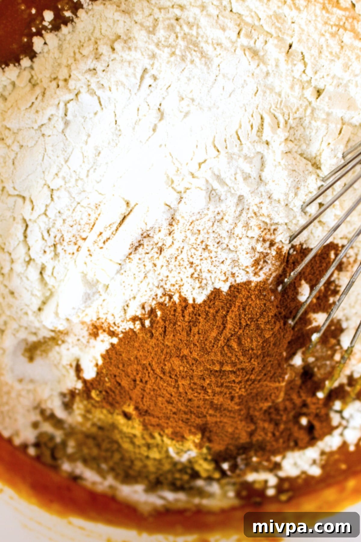 Dry ingredients being whisked into the pumpkin mixture in a bowl.
