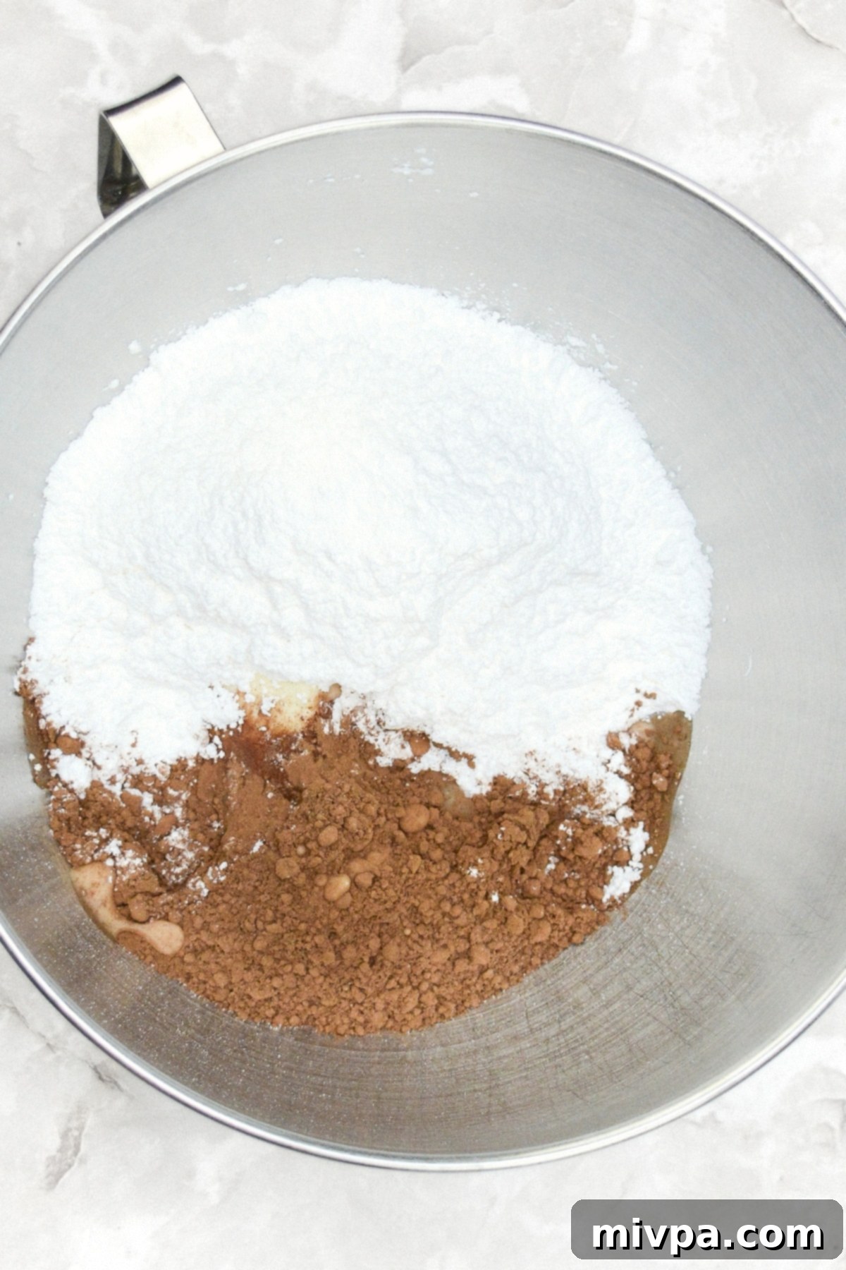 Gluten-Free Pumpkin Cupcake Recipe (Dairy-Free) Dry ingredients for chocolate frosting, including cocoa powder and powdered sugar, in a metal mixing bowl.