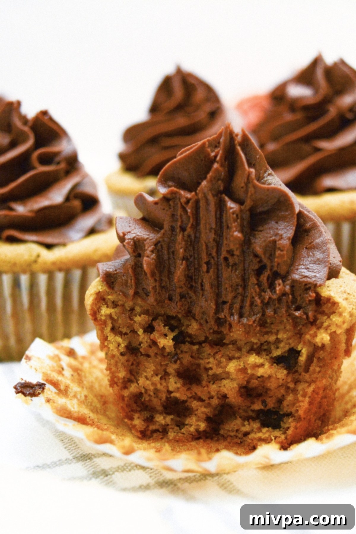 Gluten-Free Pumpkin Cupcakes (Dairy-Free) Half-eaten gluten-free pumpkin cupcakes with chocolate chips visible, showcasing their moist texture.