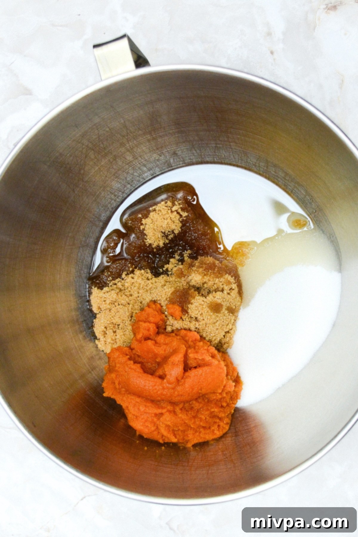 Gluten-Free Pumpkin Cupcakes with Chocolate Chips A metal bowl containing pumpkin puree, brown sugar, white sugar, and oil, being mixed.