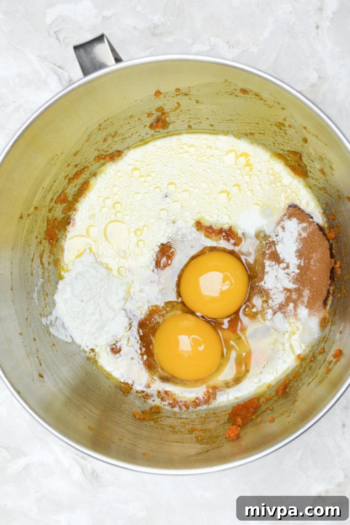 Gluten-Free Dairy-Free Pumpkin Cupcakes A metal bowl with the wet ingredients and spices for the cupcake batter, including eggs and almond milk.