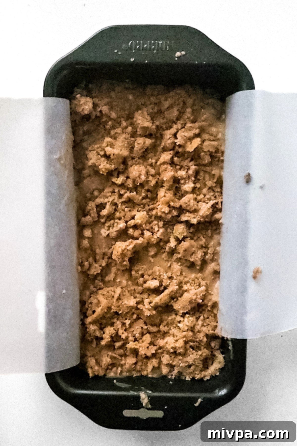 Vegan Gluten-Free Apple Bread Apple bread batter layered with crumble topping in a parchment-lined pan, ready for baking.