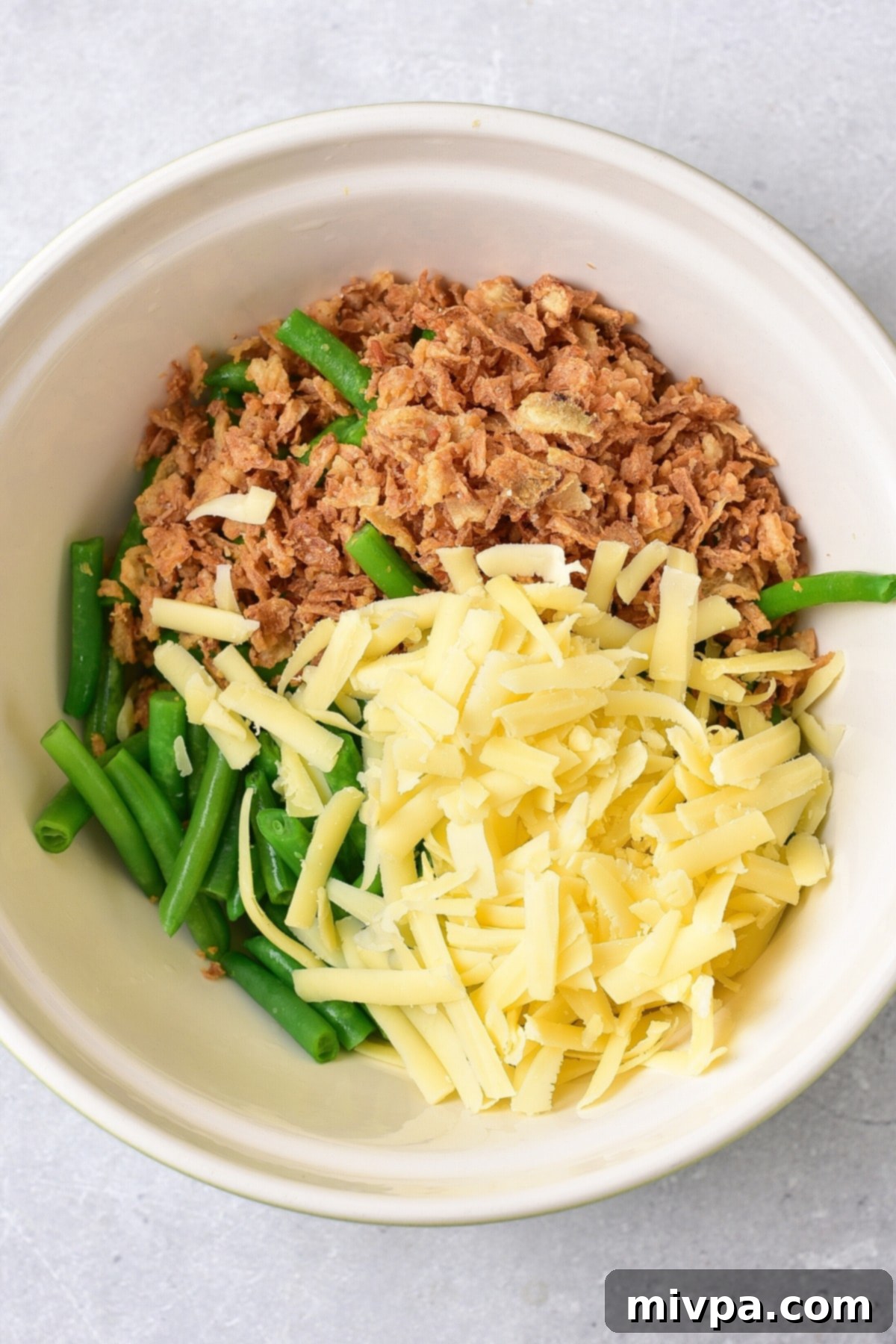 A bowl with green beans, crispy onions and shredded cheese.