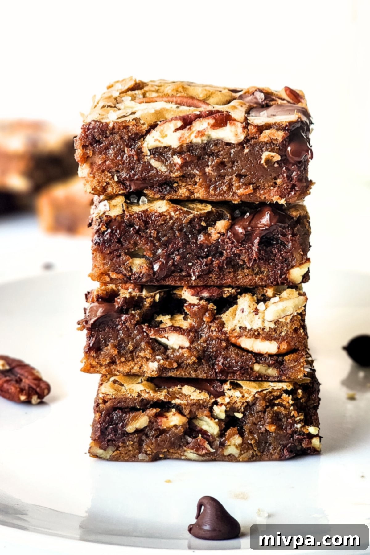A stack of golden-brown chocolate pecan bars on a white plate, highlighting their fudgy texture and visible chocolate and pecan pieces.