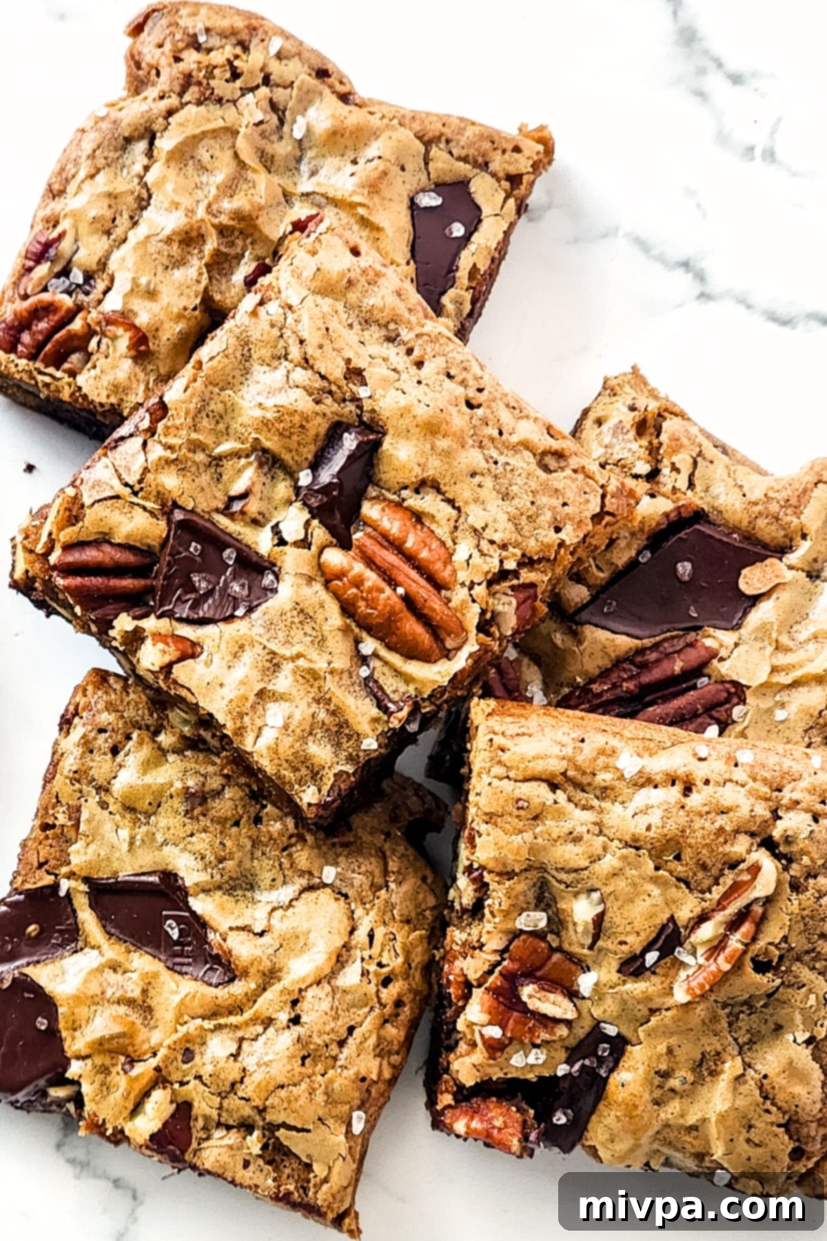 An up-close shot of chocolate pecan brownies on a marble board, showing their thick, chewy texture and abundant chocolate chunks.