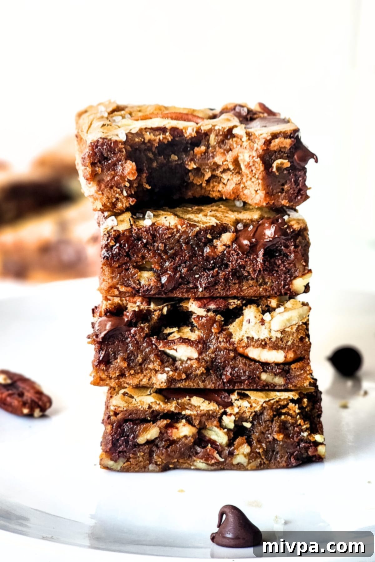 A stack of three half-eaten pecan chocolate bars on a plate, showing their rich, dense interior and crisp edges.