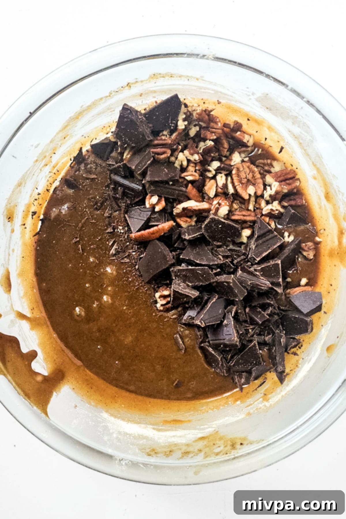 Generous amounts of chopped chocolate and pecans folded into the brown batter in a glass bowl.