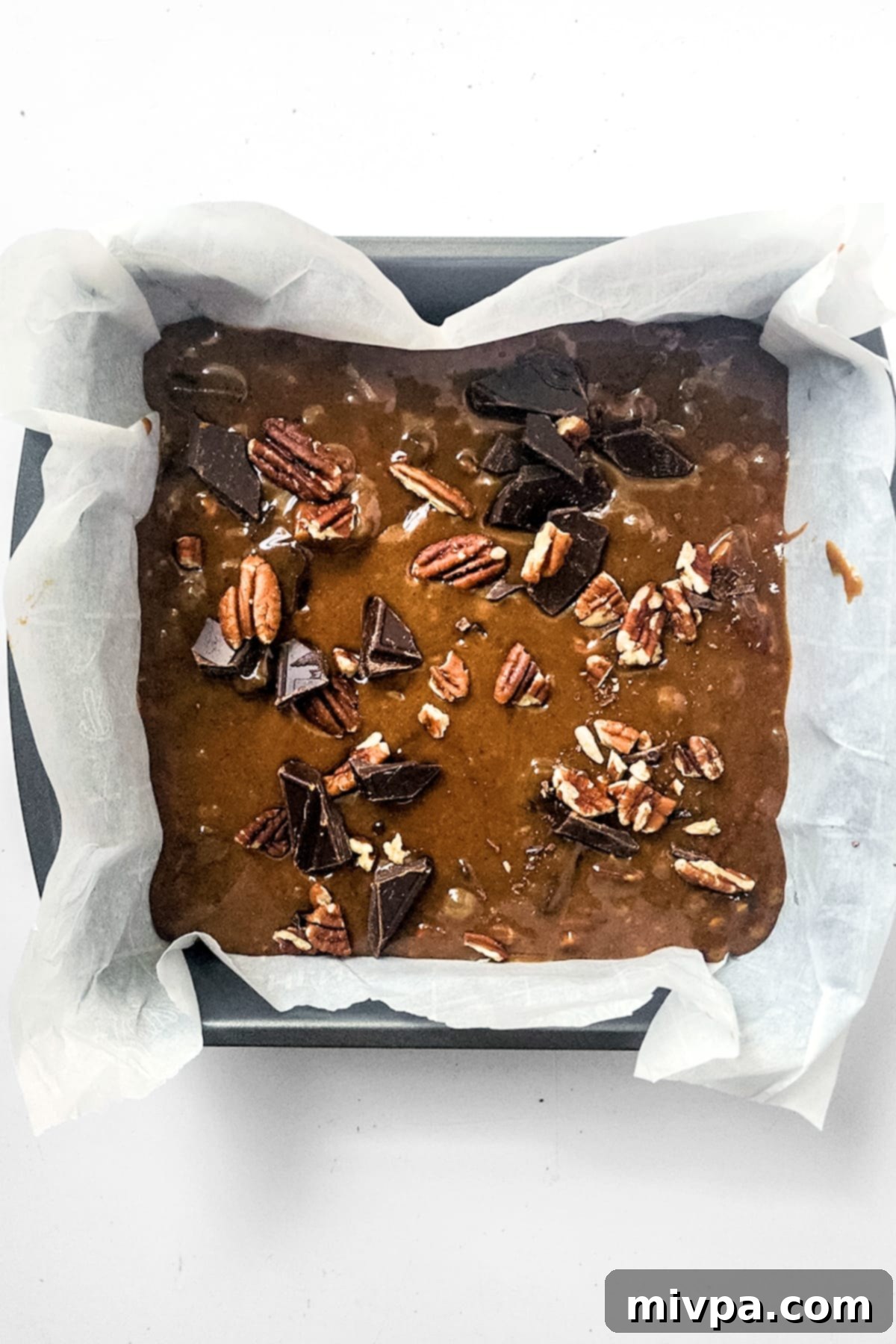 The blondie batter topped with chocolate and pecans, neatly spread in a parchment-lined baking pan.