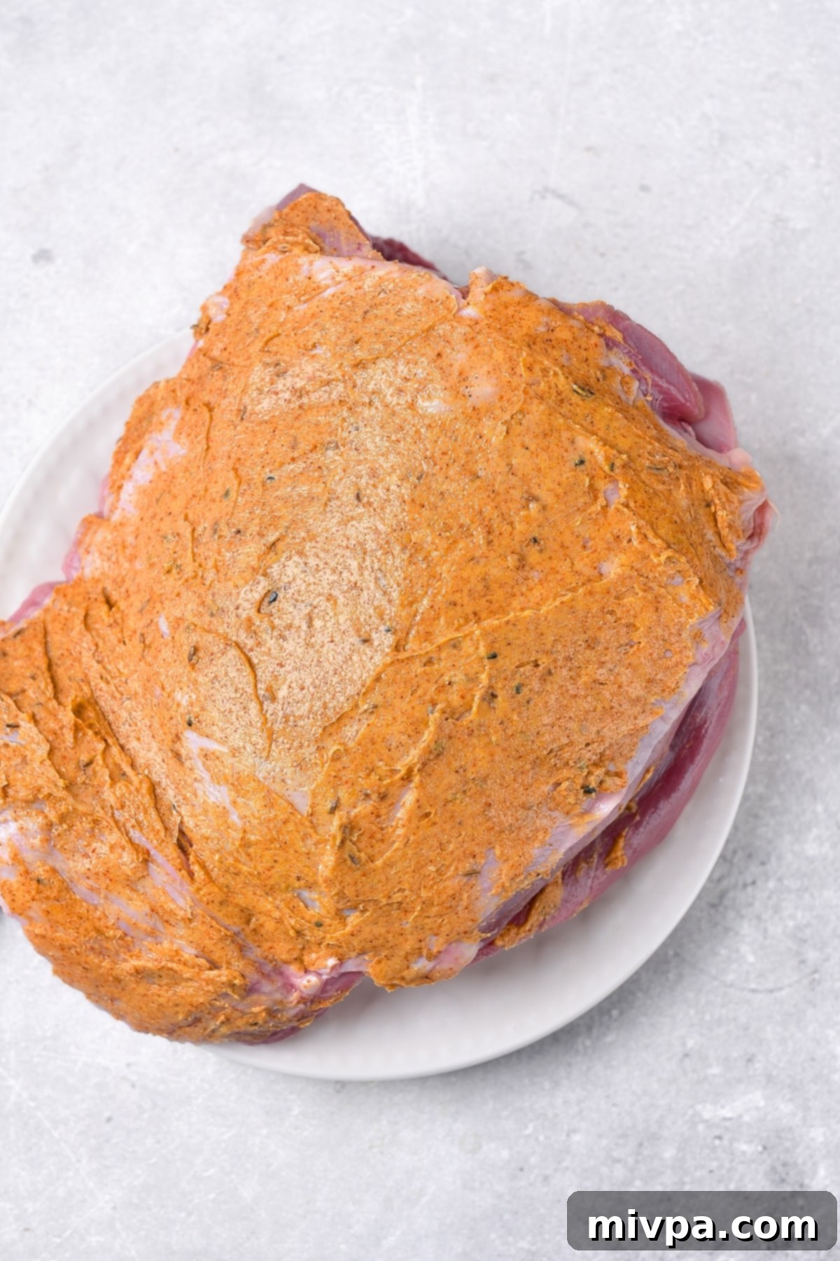 Oven Roasted Turkey Thigh Recipe (Gluten-Free, Dairy-Free) Marinated turkey thigh on a white plate, coated evenly with the butter seasoning.