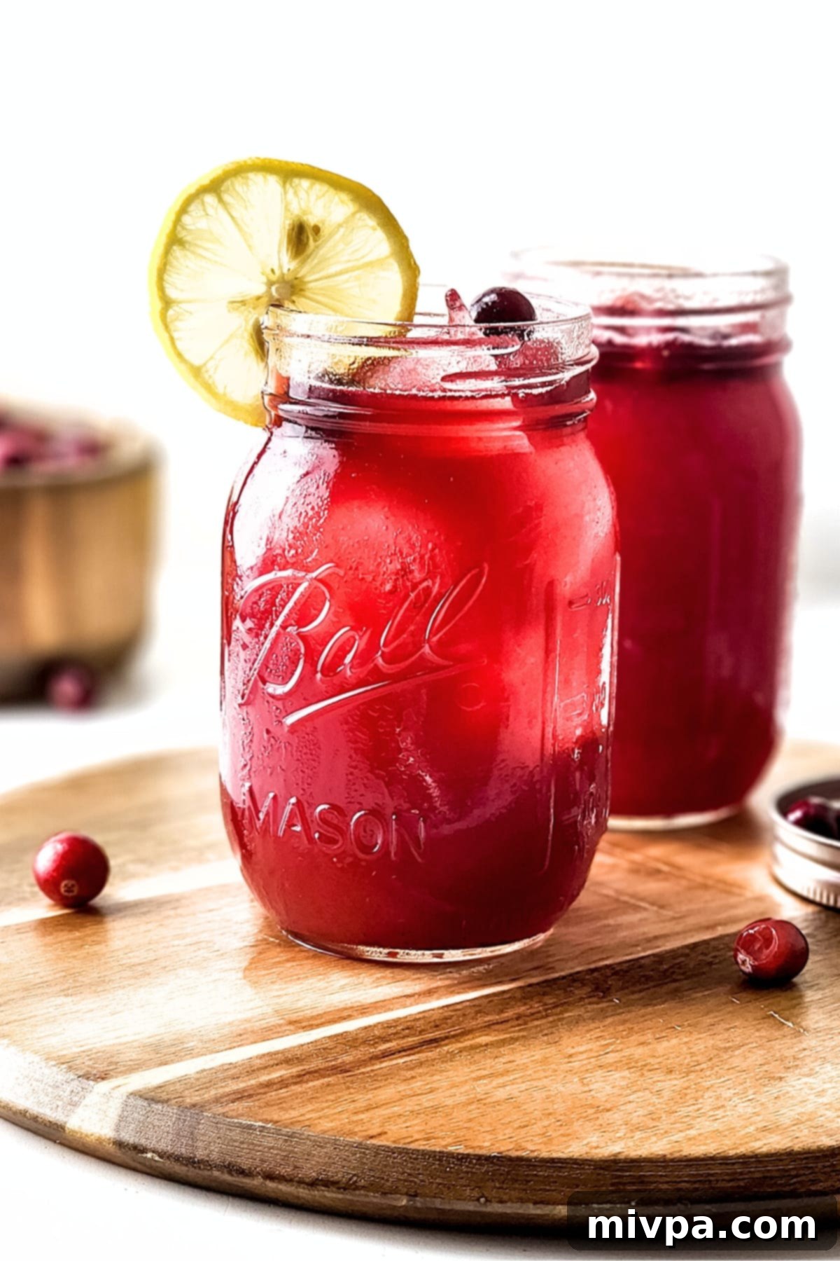 Glasses of homemade cranberry juice on wooden board, showcasing its vibrant color and freshness.