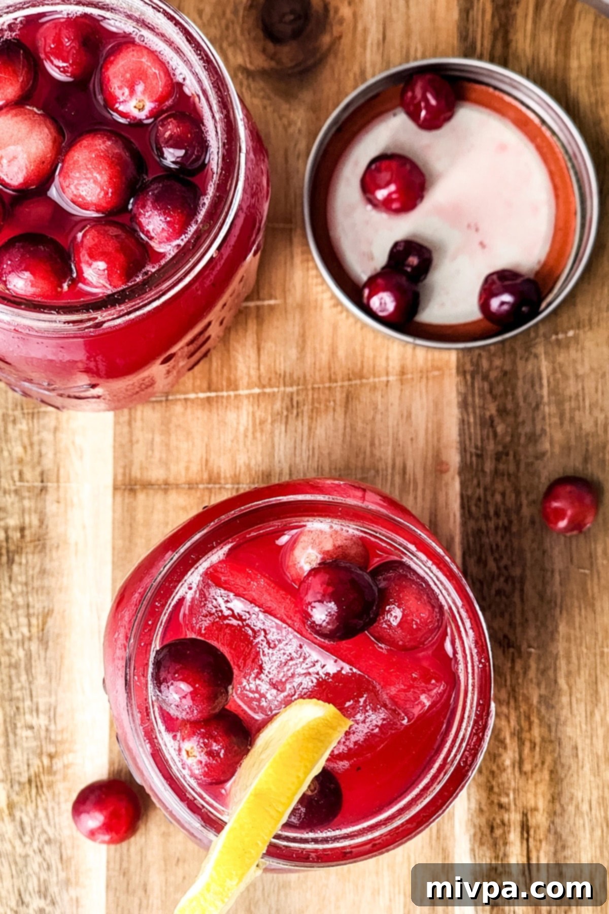 Three glasses of homemade cranberry juice on a rustic wooden board, garnished with fresh cranberries and lemon slices, ready to be served.